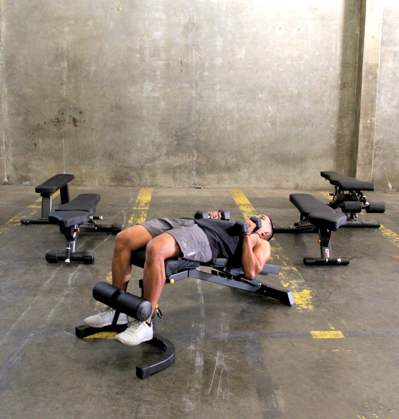 A man reclined on a bench with a weight bench nearby, indicating a moment of rest in his fitness training.