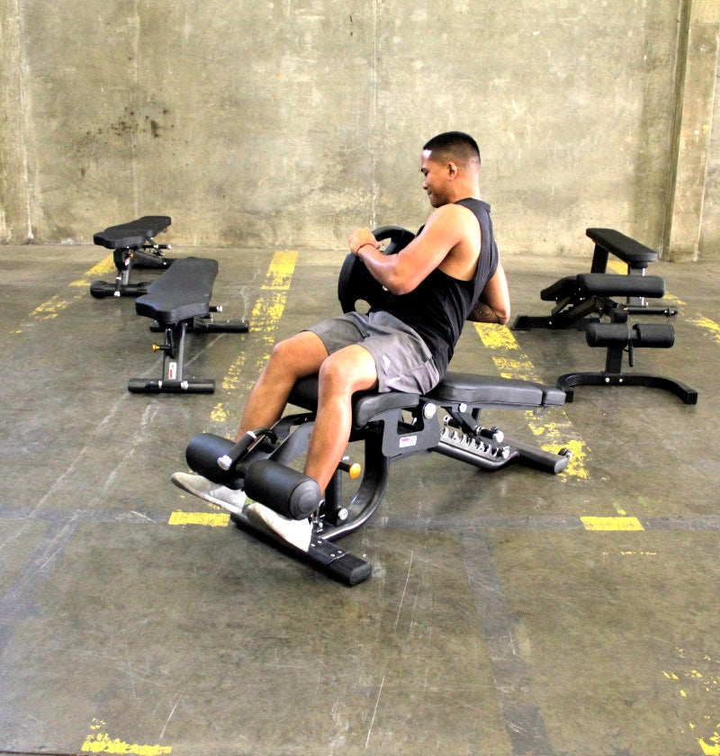 A man is seated on a bench beside a weight machine, focused on his exercise routine in a fitness environment.