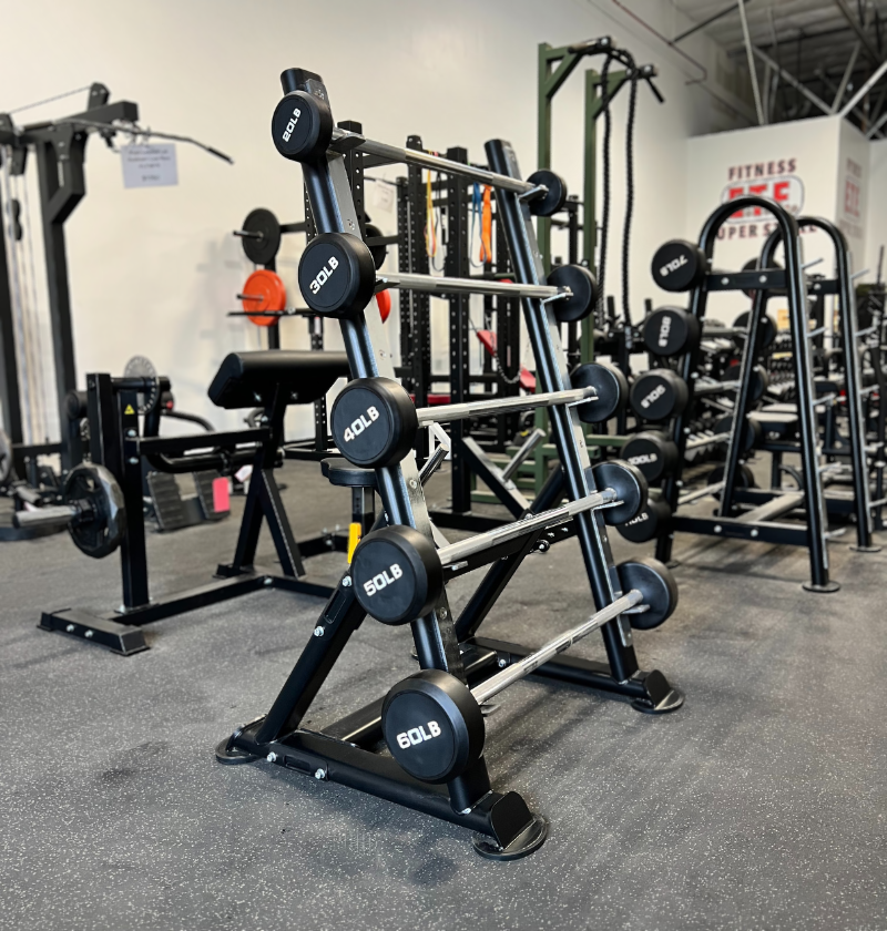 A black and silver fixed straight barbell with marked weight plates displayed on a black metal rack in a gym setting