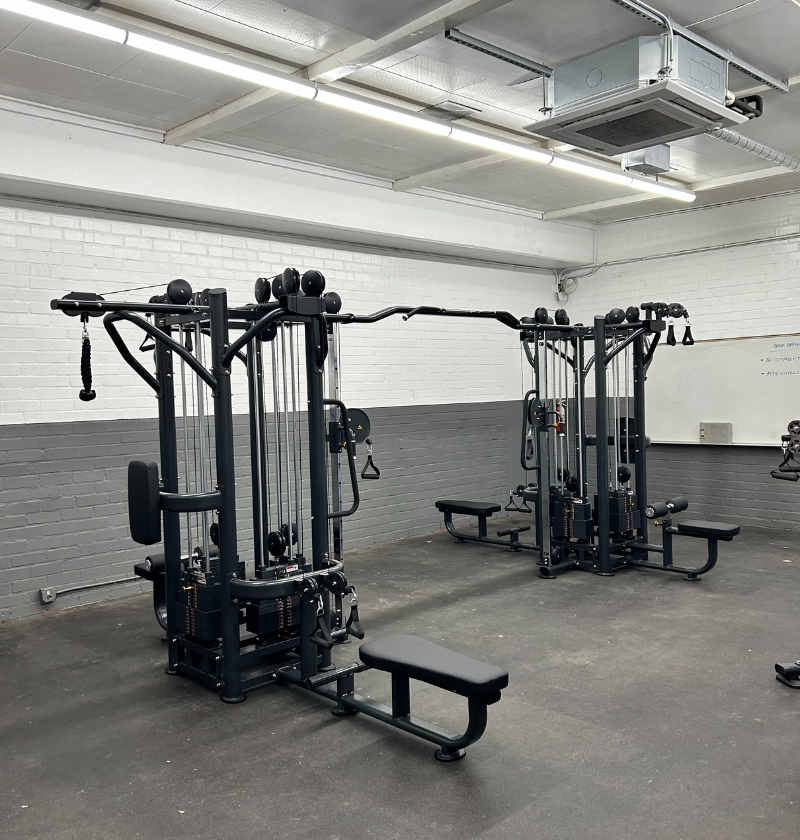 A gym space with a white wall and black workout equipment, highlighting four separate stations for exercise routines