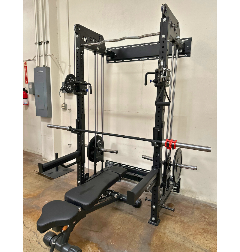 Black plate loaded functional trainer squat rack with various attachments in a warehouse setting.