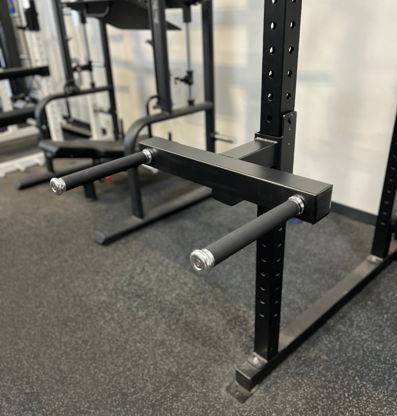 A black dip attachment for a power rack with two parallel bars and a central connecting bar, designed for upper body strength exercises.
