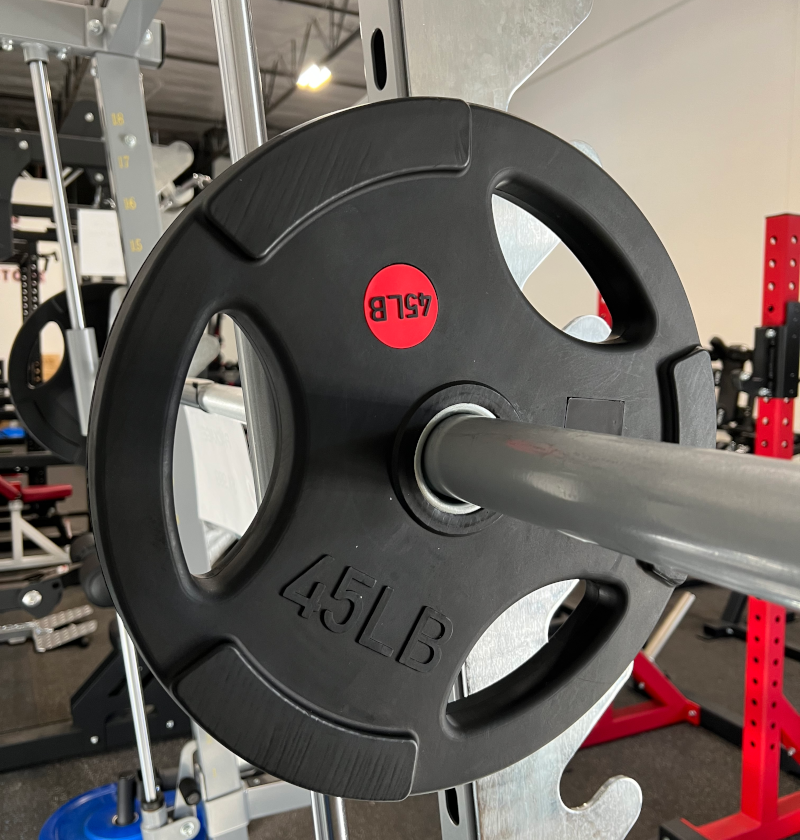A barbell centered on gym equipment, surrounded by a full set of 245lbs rubber grip plates for weight training.