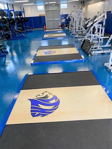 A gym featuring blue flooring and various equipment, including an Olympic lifting platform.
