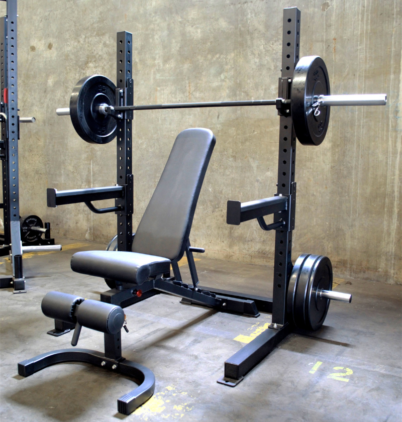 A black 6ft Basic Squat Rack with a pair of spotter arms, j-hooks, and weight peg holders, accompanied by a power bar and an adjustable bench.