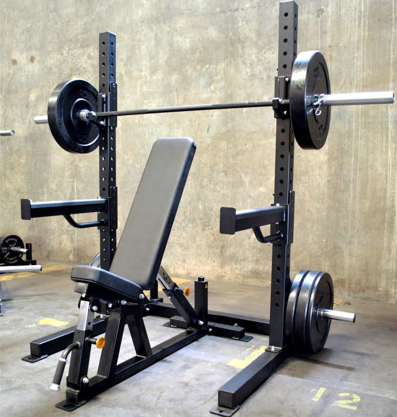 A black 6ft Basic Squat Rack with a pair of spotter arms, j-hooks, and weight peg holders, accompanied by a power bar and an adjustable bench.