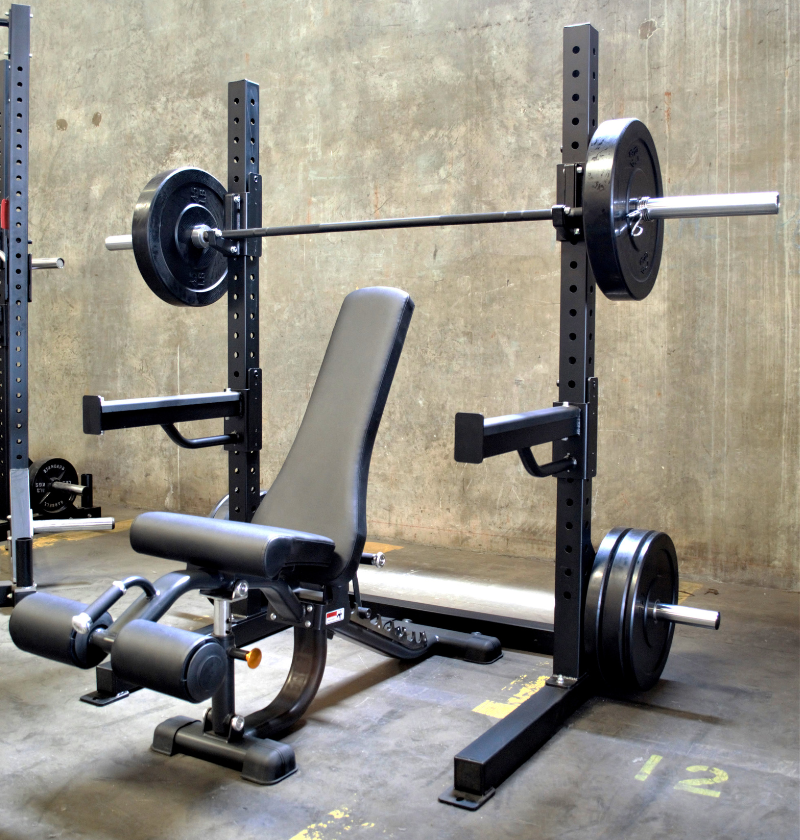 A black 6ft Basic Squat Rack with a pair of spotter arms, j-hooks, and weight peg holders, accompanied by a power bar and an adjustable bench.