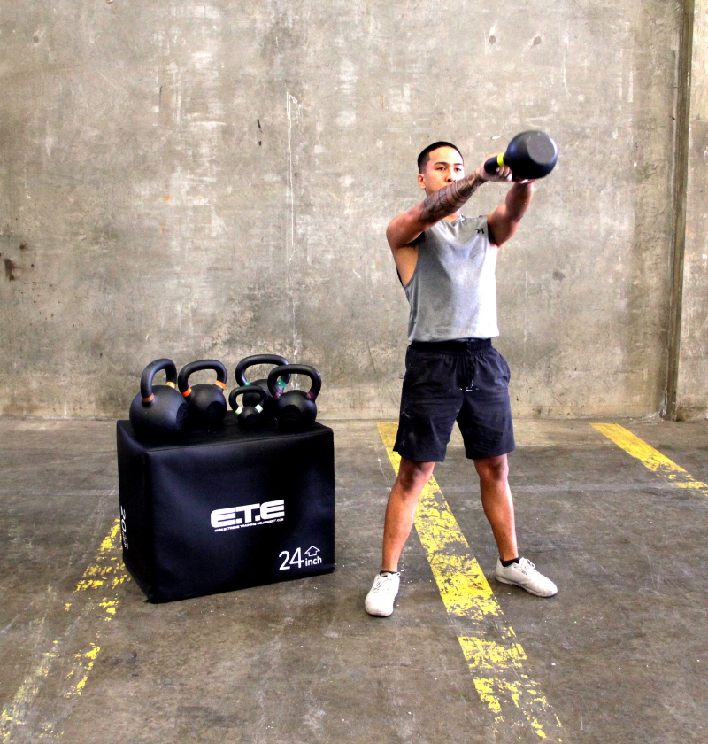 A man is lifting a kettlebell in a gym, emphasizing his commitment to physical fitness and strength training.