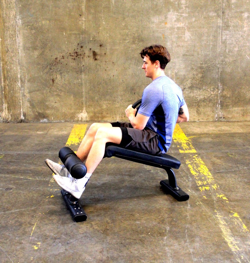 A man sits on a bench, holding a dumbbell in his right hand, focused on his workout routine.