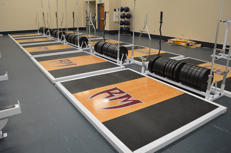 A gym featuring an Olympic lifting platform with a row of weight plates neatly arranged on the floor.
