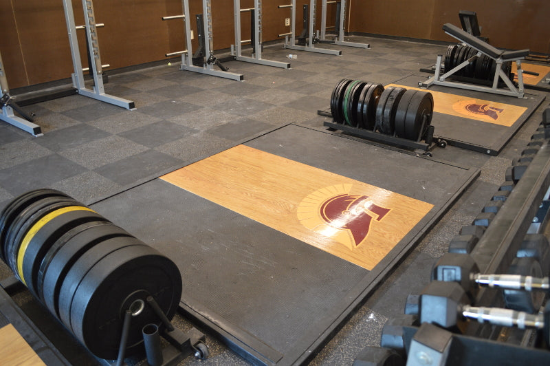 A gym featuring an Olympic lifting platform, weights, and a bench positioned centrally for workouts.