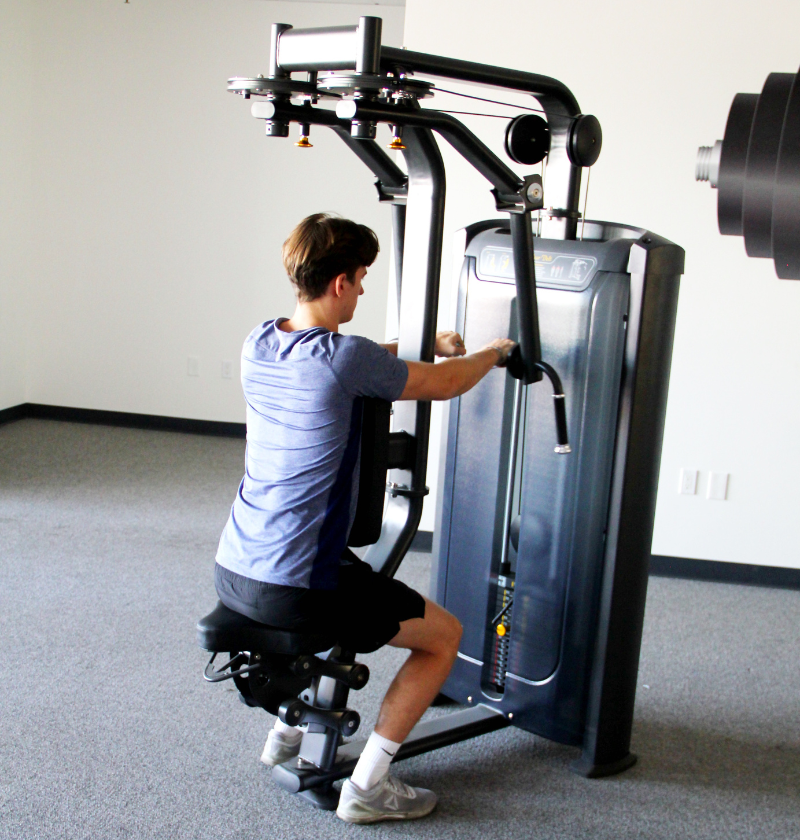 A man exercises on the Pec Fly Rear Delt gym machine in a fitness room.