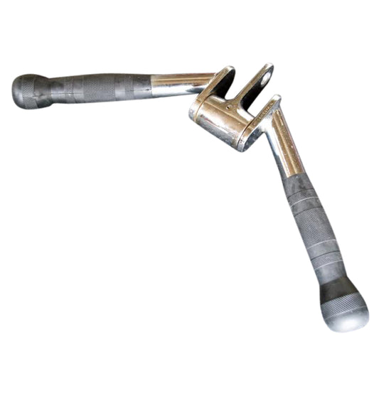 A metal pipe wrench with two handles, designed for gripping and turning pipes, shown in a workshop setting.