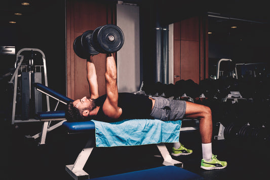 A man performs a bench press with a dumbbell on an adjustable workout bench, suitable for beginners and experts.