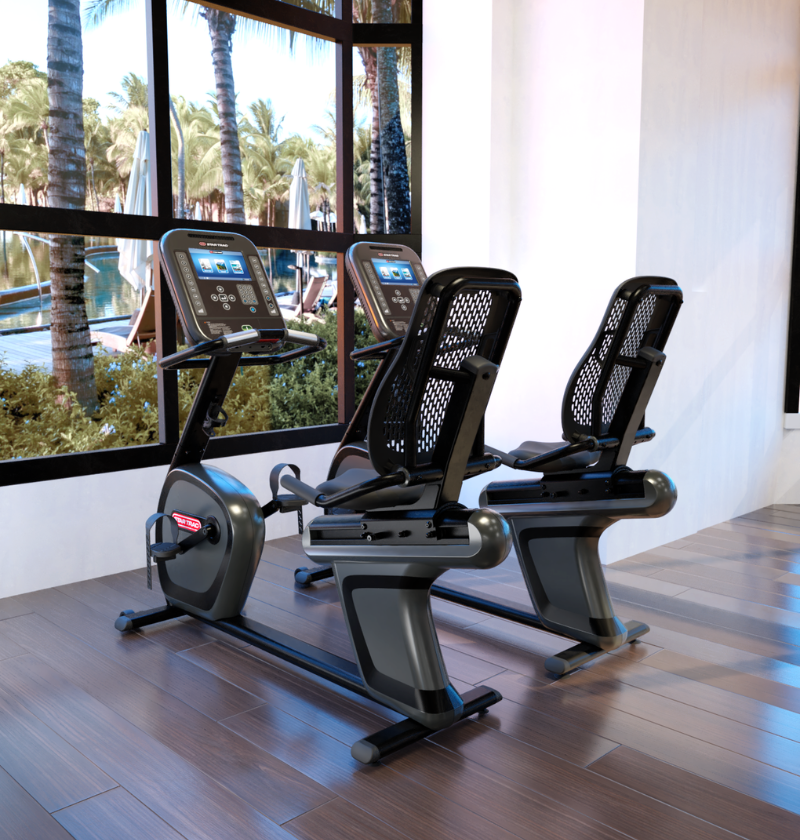 Three star trac 4 series recumbent bikes in a modern indoor setting with large windows showing outdoor greenery.