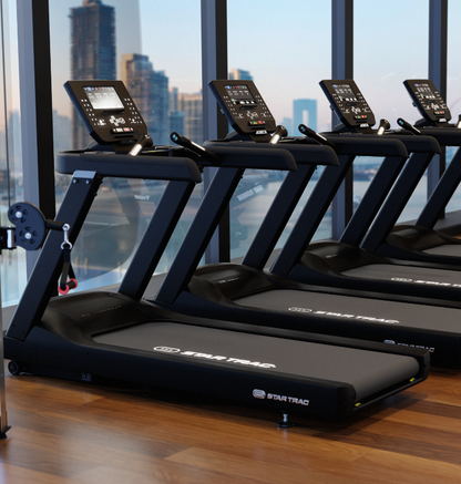 Row of star trac treadmills in a gym with a cityscape view through large windows.