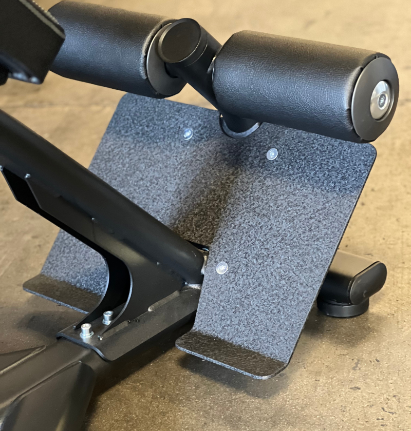 Close-up of a black 45 degree hyperextension machine with a foot plate on a beige floor.