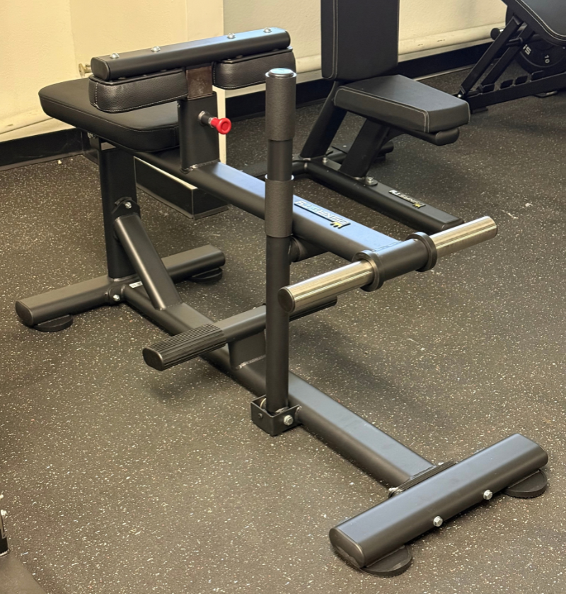 A black plate loaded seated calf machine photographed in a gym setting on a speckled gray floor.