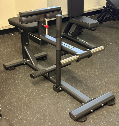 A black plate loaded seated calf machine photographed in a gym setting on a speckled gray floor.