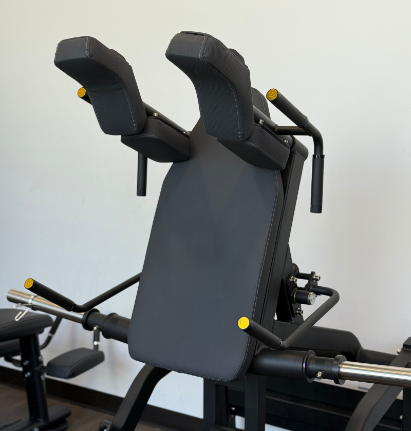 Front squat machine with black padding and metal components on a light gray background in a showroom.