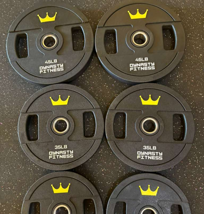 Set of black urethane weight plates with yellow crowns and 'Dynasty Fitness' branding on a dark speckled surface.