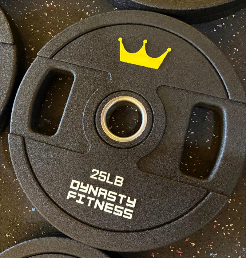 Set of black urethane weight plates with yellow crowns and 'Dynasty Fitness' branding on a dark speckled surface.