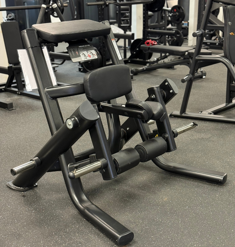 Black plate loaded kneeling leg curl machine on black flooring.