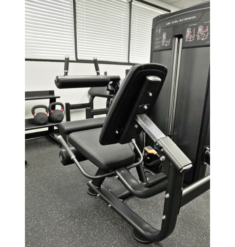Leg extension leg curl Gym machine in a fitness showroom with weights and equipment in the background